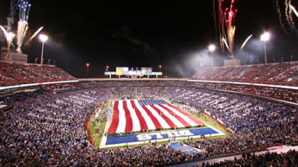 Men wave flags on the field before the start of an NFL football