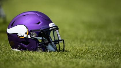 A Minnesota Vikings helmet rests on purple turf as players take