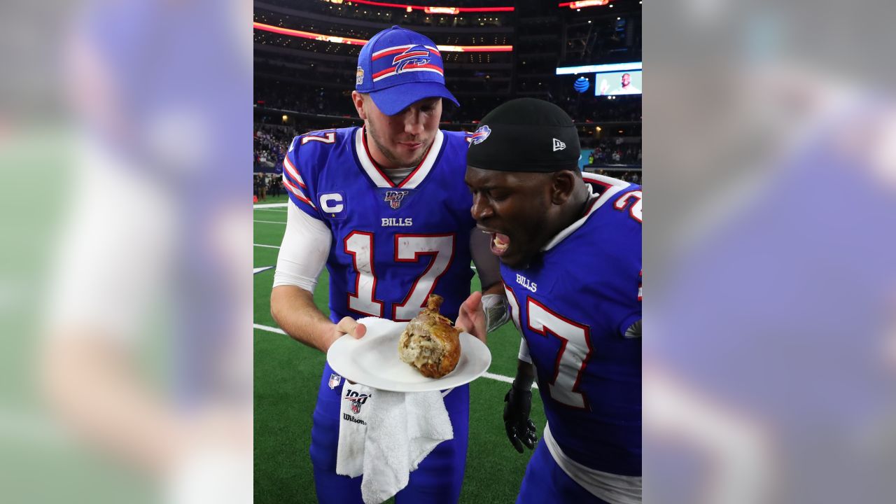 Buffalo Bills quarterback Josh Allen holds a plate with a turkey leg as  cornerback Tre'Davious White (27) leans over to take a bite as they  participate in a post game broadcast interview