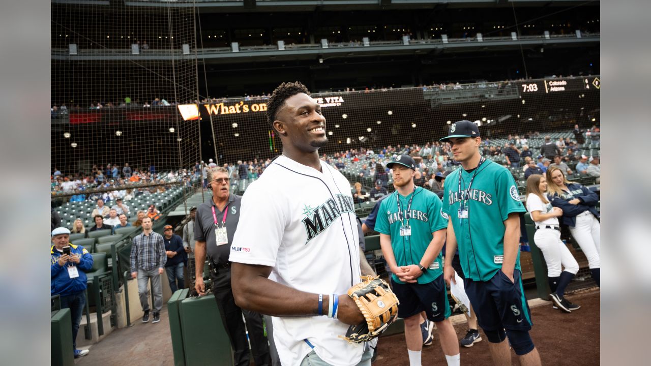 Seattle Seahawks rookie wide receiver DK Metcalf throws out the first pitch  at a baseball game between the Seattle Mariners and the Baltimore Orioles,  as other rookies from the NFL football team