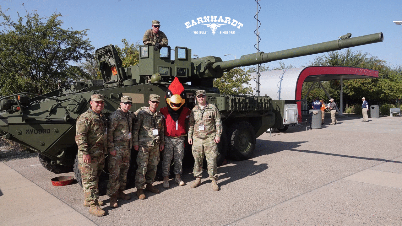 Big Red poses with members of the military in front of a tank