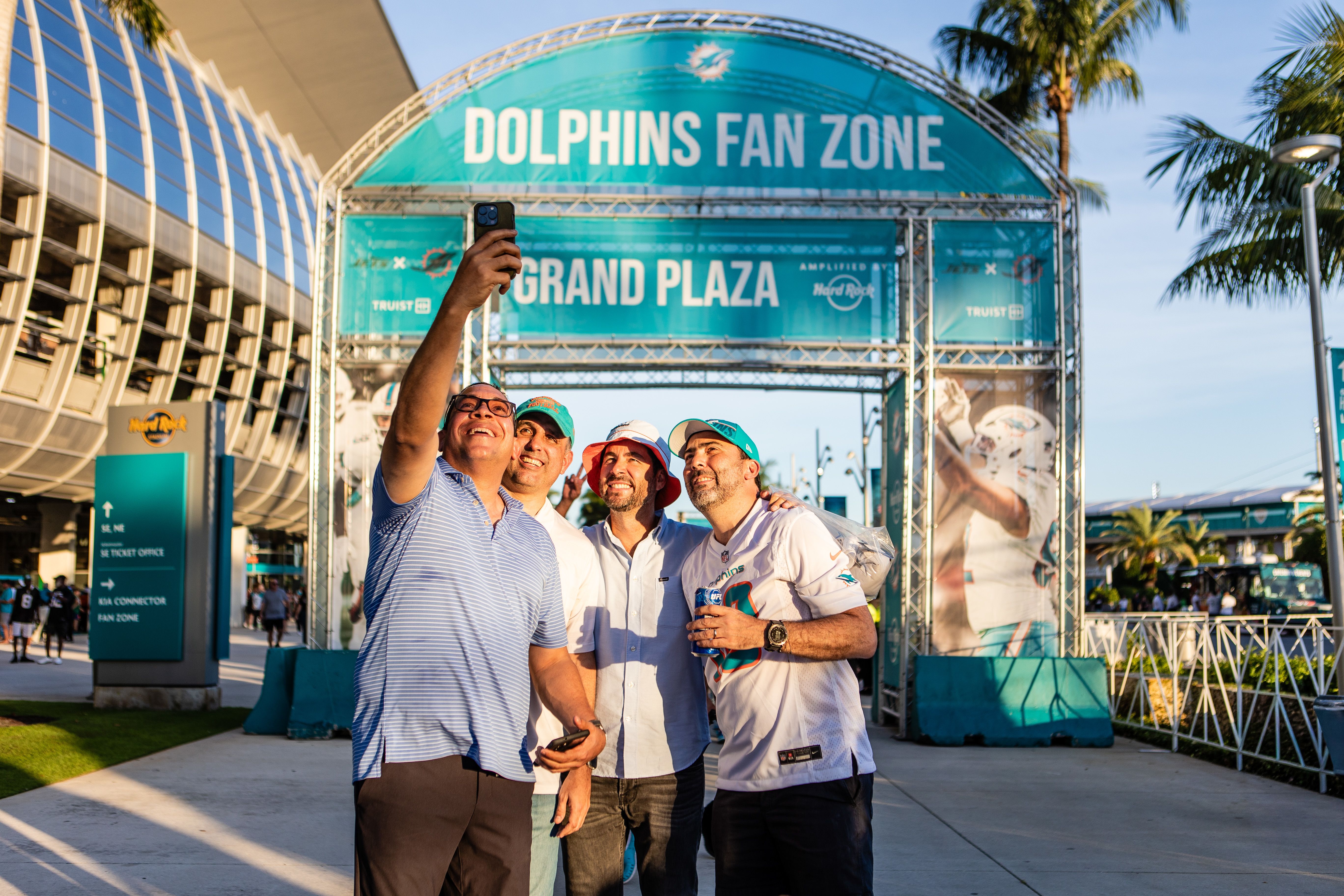 Fans taking a selfie in front of Dolphins fan zone grand plaza sign during an NFL football game against the New York Jets on Sunday, March 30, 2025 in Miami Gardens, Fla. (Isabella Frias/Miami Dolphins via AP)