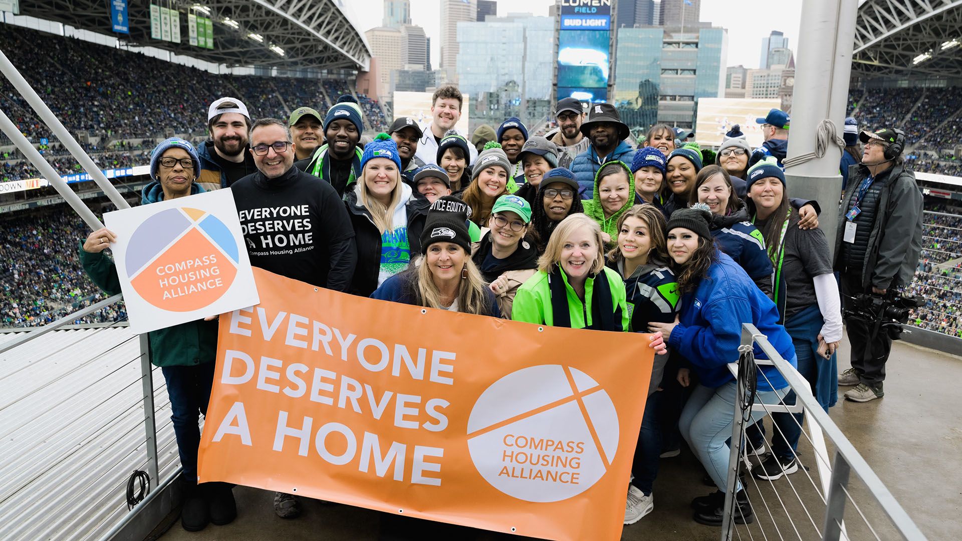 Group of people stand behind a sign reading "Everyone Deserves a Home"