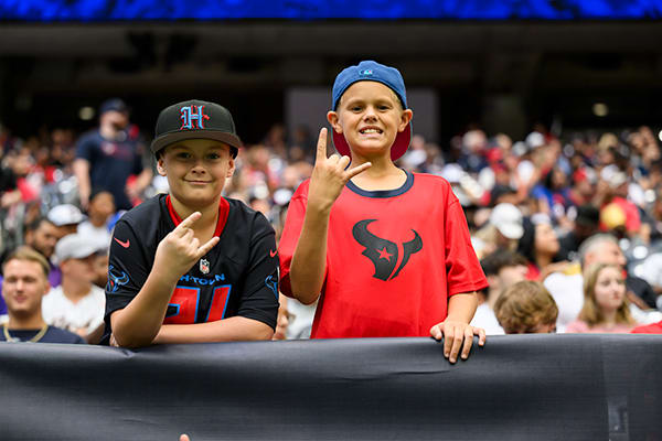Two young Texans fans in team gear throwing bull horns from the stands during a game.