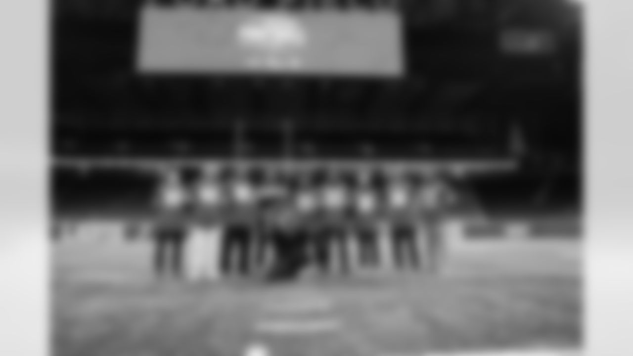 Detroit Lions wide receiver Tom Kennedy (85), Detroit Lions long snapper Hogan Hatten (49), Detroit Lions edge rusher Al-Quadin Muhammad (96), Lions Legend Martell Webb, Detroit Lions running back Jacob Saylors (25), Detroit Lions cornerback Rock Ya-Sin (23), Detroit Lions cornerback Khalil Dorsey (30), Lions Legend Ross Weaver, Lions Legend Alex Lewis (59) and Detroit Lions Mascot Roary pose for a group photo during the Inspire Change Football Clinic at Ford Field on Dec. 9, 2025 in Detroit. (Izzy Rincon/Detroit Lions)