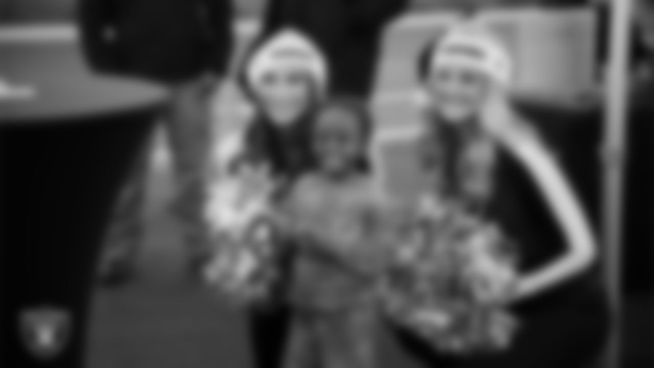 Raiderettes Madisyn and Jessica pose for a photo with a child during the Raiders Holiday Salute at Nellis Air Force Base - Coral Academy.